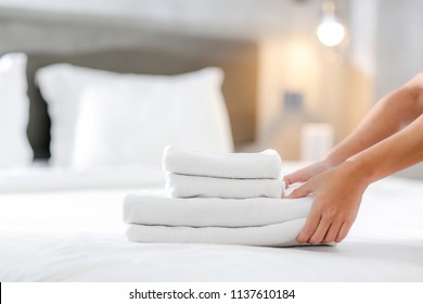 Close-up of hands putting stack of fresh white bath towels on the bed sheet. Room service maid cleaning hotel room. - Shutterstock ID 1137610184