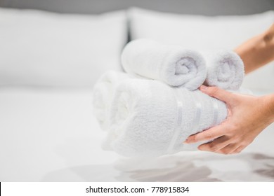 Close-up of hands putting stack of fresh white bath towels on the bed sheet. Room service maid cleaning hotel room.

