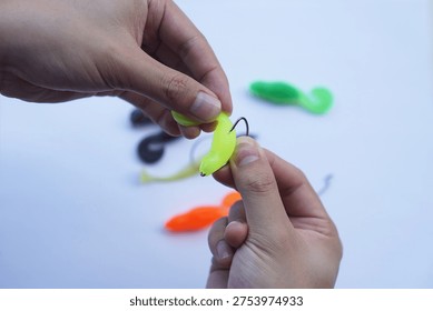 Close-up of hands rigging a soft plastic fishing lure onto a hook on a clean white background. Concept of angling preparation, sport fishing equipment, bait rigging technique and recreational fishing gear.                              