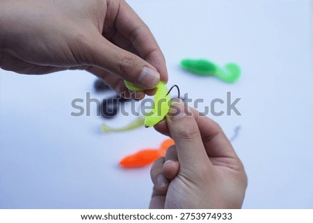 Close-up of hands rigging a soft plastic fishing lure onto a hook on a clean white background. Concept of angling preparation, sport fishing equipment, bait rigging technique and recreational fishing gear.                              