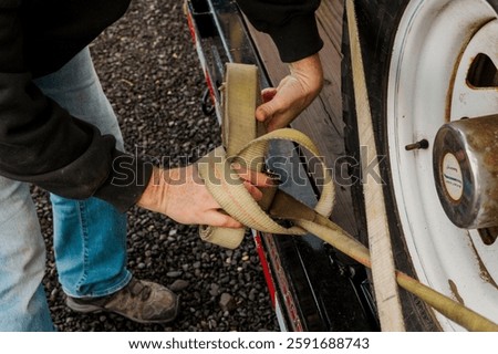 Close-up of hands securing a ratchet strap on a trailer wheel