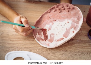 Close-up of hands. Selective focus. A young woman artist painting her clay product, a plate, in brown. Preparing for final burning. Brush on a colorless plate to make it bright and colorful later. - Powered by Shutterstock