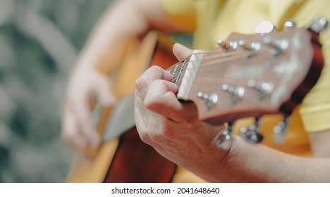 Closeup hands of senior woman hold acoustic guitar neck play songs. Old musician press fingers on metal strings on fingerboards practicing melody chords in leisure time. Happy aged guitarist lifestyle