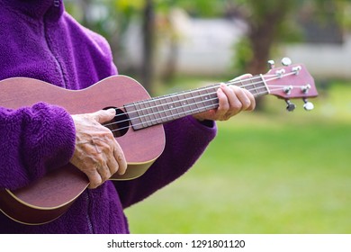Close-up of hands senior woman holding ukulele while standing in a garden. Space for text. Concept of aged people and relaxation