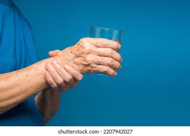 Close-up Of Hands Senior Woman Trying To Hold A Glass Of Water. Causes Of Handshaking Include Parkinson's Disease, Stroke, Or Brain Injury. Mental Health Neurological Disorder