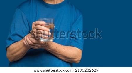 Close-up of hands senior woman trying to hold a glass of water. Causes of hand shaking include Parkinson's disease, stroke, or brain injury. Mental health neurological disorder