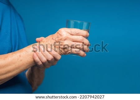 Close-up of hands senior woman trying to hold a glass of water. Causes of handshaking include Parkinson's disease, stroke, or brain injury. Mental health neurological disorder