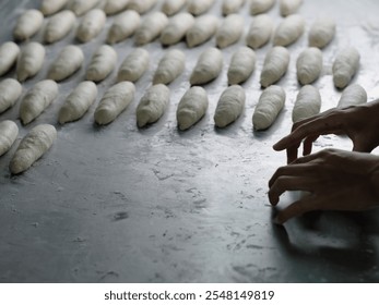 Close-up of hands shaping dough pieces on a metallic table. The image captures the precision and artistry involved in bread making, emphasizing fresh production in a professional bakery. - Powered by Shutterstock