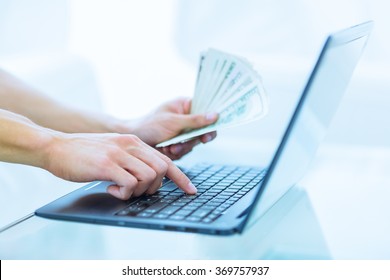 Close-up of hands shopping/paying online using laptop while holding US dollars.. - Powered by Shutterstock