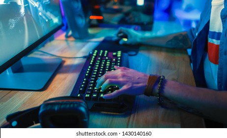 Close-Up Hands Shot Showing a Gamer Using the Keyboard while Playing an Online Shooter Video Game. Keyboard has Green Neon Lights in Buttons. Gamer is Wearing a Bracelet. Room is Dark. - Powered by Shutterstock