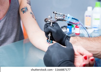 Close-up of the hands of a skilled tattoo artist wearing black gloves while setting a sterile machine for tattooing in a modern studio