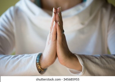 Close-up of hands of sporty young beautiful woman in white clothes meditating indoors, focus on arms in Namaste gesture