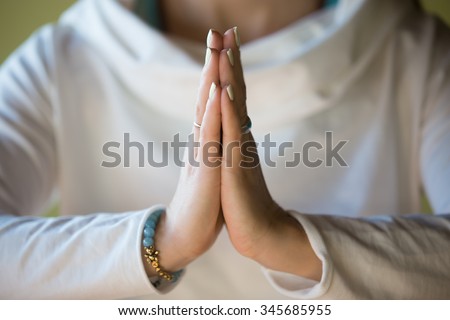Close-up of hands of sporty young beautiful woman in white clothes meditating indoors, focus on arms in Namaste gesture