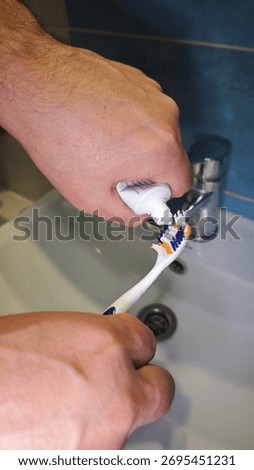Close-up of hands squeezing toothpaste onto a toothbrush over a bathroom sink. The image represents hygiene, freshness, and daily morning routine
