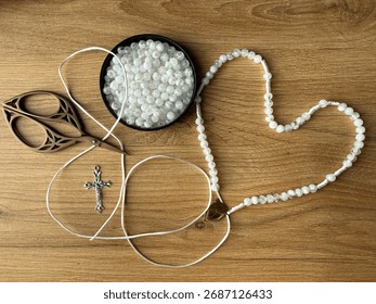 Close-up of hands stringing white beads onto thread to create a handmade rosary. Creative religious craft project representing dedication and mindfulness.