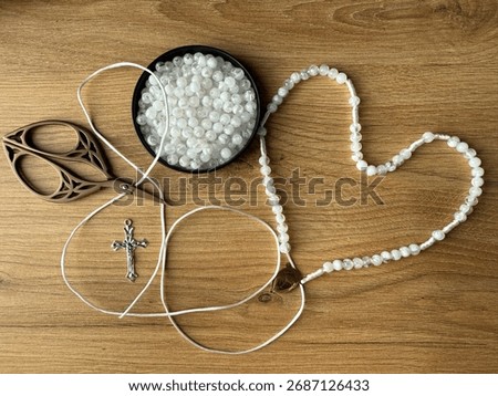 Close-up of hands stringing white beads onto thread to create a handmade rosary. Creative religious craft project representing dedication and mindfulness.