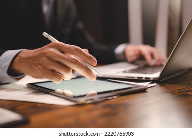 Closeup of hands of a successful business man and entrepreneur in formal clothing sitting in modern lighted office while holding pen and using digital tablet and reading document and making edits - Shutterstock ID 2220765903