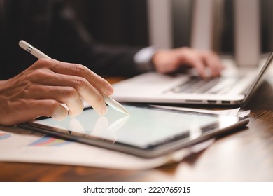 Closeup of hands of a successful business man and entrepreneur in formal clothing sitting in modern lighted office while holding pen and using digital tablet and reading document and making edits - Shutterstock ID 2220765915