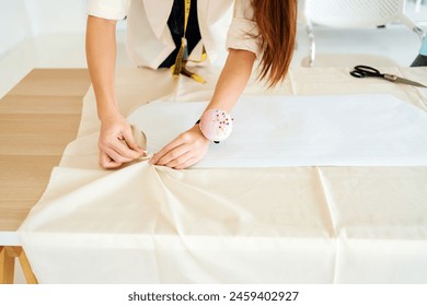 Close-up hands of a tailor or fashion designer woman seamstress pinning up the paper pattern on the fabric with a pin cushion on her wrist. A woman tailor sews clothes with her own hands. - Powered by Shutterstock