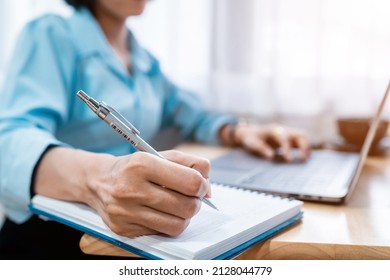 Close-up of hands Taking written Notes to on notebook and freelance business female casual working with laptop computer ,warm milk cup in coffee shop like,Distance job communication concept