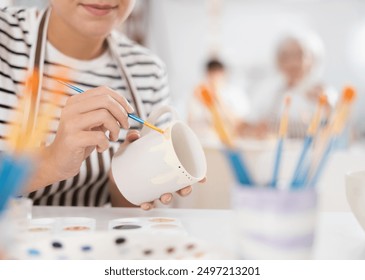 Closeup of hands of talented female artisan creating own unique ceramic items in pottery workshop, painting mug with engobe and brush. Craft activity concept - Powered by Shutterstock