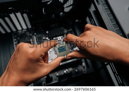 Close-up hands of technician inserting processor into desktop motherboard during computer hardware upgrade or repair process at dark workshop. Concept of desktop PC maintenance and service.