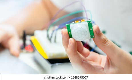 Closeup, Hands of teenage student hold PIR sensor connected to breadboard and microcontroller with colorful wires, learn, code and test motion detection in robotics school project on STEM education. - Shutterstock ID 1648395007
