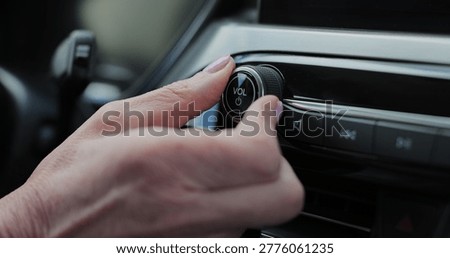 Close-up of hands turning volume button of car radio. Woman driving car. Listen to music while driving