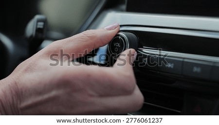 Close-up of hands turning volume button of car radio. Woman driving car. Listen to music while driving