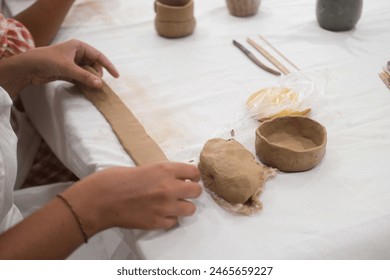 A close-up of the hands of two diverse women Caucasian and African American who are sitting in a art workshop in aprons and making mugs from pottery clay. They form a cup out of clay and communicate. - Powered by Shutterstock