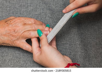 Close-up Of The Hands Of Two Unrecognizable Women, One Young And One Old, Having A Manicure. The Young Woman Is Filing The Underside Of The Older Woman's Nails With A Nail File.