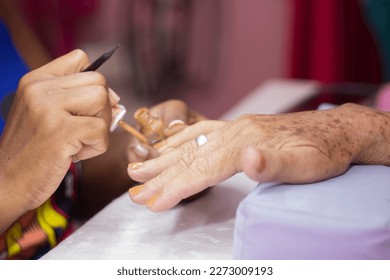 Close-up of the hands of two unrecognizable women. Manicure painting on the older woman's nails. - Shutterstock ID 2273009193