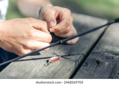 Closeup of hands tying a fishing knot on a fishing lure on a wooden table with fishing rod in sunshine. Summer in Norway. - Powered by Shutterstock