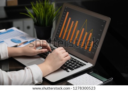 Close-up of hands typing on laptop with blank black screen next to charts and calculator
