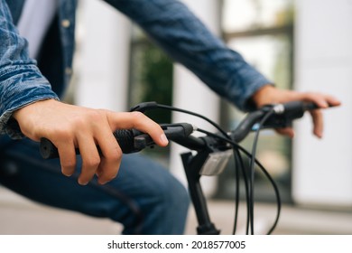 Close-up hands of unrecognizable cyclist male pressing handlebars on handlebars of bicycle outdoors on blurred background. Side clsoep view of bicyclist checking work of braking system of bike.