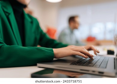 Close-up hands of unrecognizable female programmer typing program code on laptop keyboard in coworking. Closeup of young copywriter writing text working in big modern corporate office with coworkers.