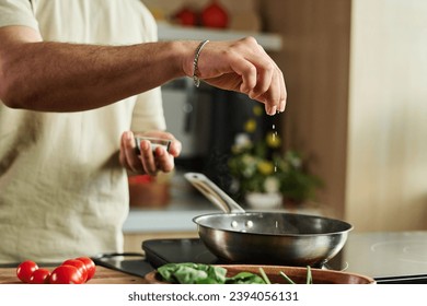 Closeup of hands of unrecognizable man adding salt to meal in pan on kitchen stove
