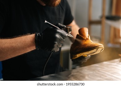 Close-up hands of unrecognizable shoemaker wearing black gloves spraying paint of light brown leather shoes. Concept of cobbler artisan repairing and restoration work in shoe repair shop. - Powered by Shutterstock