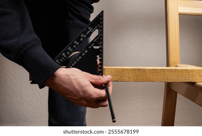 Close-up of hands using a black square ruler and pencil to mark precise measurements on a wooden plank. Highlights woodworking and DIY craftsmanship. Horizontal composition - Powered by Shutterstock