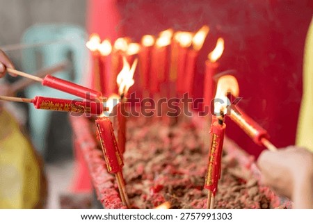 Closeup of hands using burning sticks to light rows of standing red Chinese prayer candles in a tray of melted wax.
