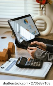 Close-up of hands using a calculator and smartphone on financial documents at a home office desk, symbolizing cost calculation, budgeting, real estate finance, and investment planning.