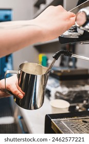 close-up of a person’s hands using an espresso machine to steam milk in a stainless steel pitcher, likely for preparing a coffee beverage. The focus on the hands and the steaming process