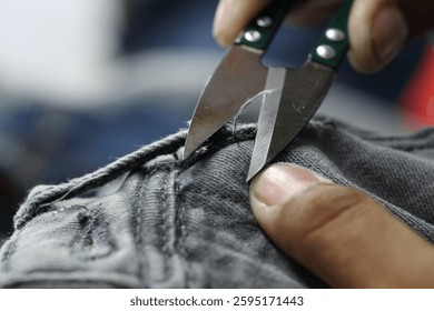 A close-up of hands using fabric scissors to cut denim material, showcasing the craftsmanship and precision in garment manufacturing.
