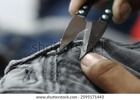 A close-up of hands using fabric scissors to cut denim material, showcasing the craftsmanship and precision in garment manufacturing.