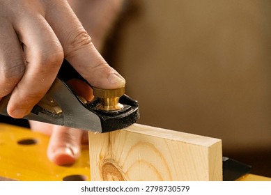 Close-up of hands using a hand plane to smooth a wooden board. Traditional woodworking process with wood shavings, craftsmanship and DIY carpentry concept