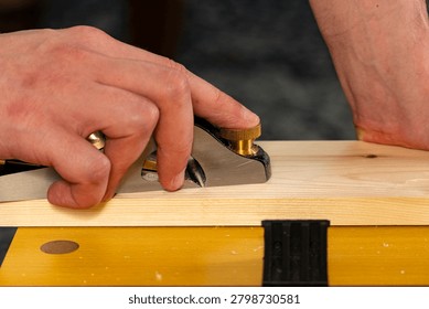 Close-up of hands using a hand plane to smooth a wooden board. Traditional woodworking process with wood shavings, craftsmanship and DIY carpentry concept
