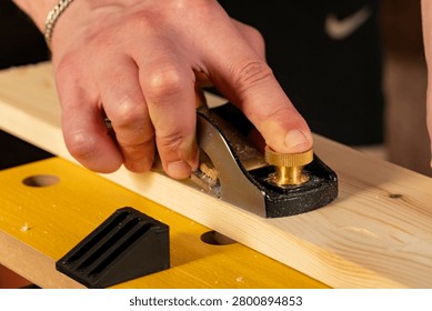 Close-up of hands using a hand plane to smooth a wooden board. Traditional woodworking process with wood shavings, craftsmanship and DIY carpentry concept