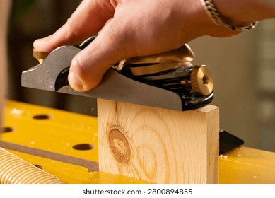 Close-up of hands using a hand plane to smooth a wooden board. Traditional woodworking process with wood shavings, craftsmanship and DIY carpentry concept