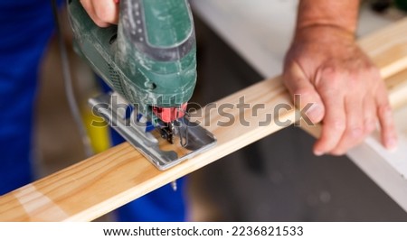 Closeup of hands using a jigsaw machine on wooden plank at the workshop, banner