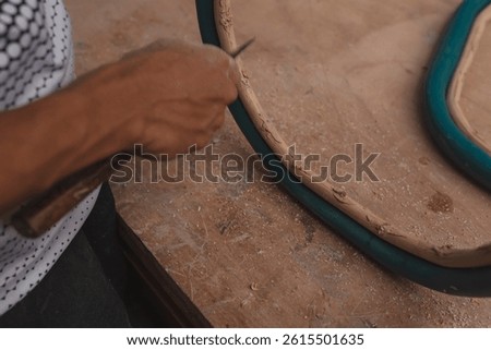 Close-up of hands using a knife or chisel to remove dried epoxy or filler from a curved wooden chair frame during furniture restoration.